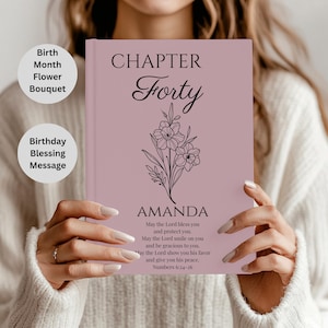 May include: A mauve-colored book with the words "CHAPTER Forty" and the name "AMANDA" in black script. A floral bouquet illustration is below the text. The book also includes the text "Birth Month Flower Bouquet" and "Birthday Blessing Message".