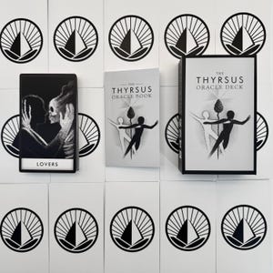May include: The Thyrsus Oracle Deck set includes a black and white card box, a guidebook titled The Thyrsus Oracle Book, and a single card labeled Lovers featuring a silhouette of two figures. The background consists of white cards with a black sun icon.