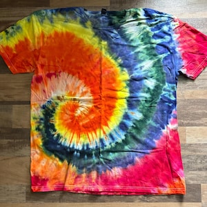 May include: A vibrant tie-dye t-shirt with a spiral design. The shirt features a blend of colors, including yellow, orange, red, blue, and green. The short-sleeved shirt is made of a soft material and is suitable for casual wear.
