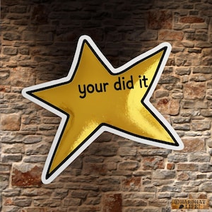 May include: A gold star sticker with the words "your did it" in black text. The star has a black outline and a white border. The sticker is against a brick wall background.