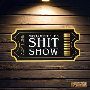 May include: A black and gold ticket with the text "Welcome to the Shit Show" and "Admit One" printed on it. The ticket is on a wood background.