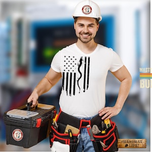 May include: A white t-shirt featuring a black graphic of the American flag with a dragon silhouette replacing the stripes. The shirt is worn with a white hard hat, blue jeans, and a black tool belt filled with various tools and a black toolbox.