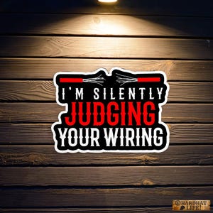 May include: A black and white sticker with red text that says "I'm silently judging your wiring". The sticker is on a wooden background.