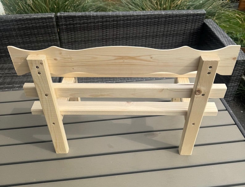 Puede incluir: Un peque&ntilde;o banco de madera sin terminar con un respaldo decorativo festoneado. El banco est&aacute; construido con madera de color claro y presenta un dise&ntilde;o simple y robusto con uniones visibles. Ideal para uso en interiores o exteriores.