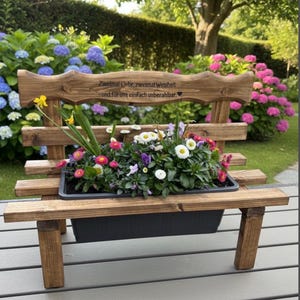 Puede incluir: Banco de jard&iacute;n de madera con jardinera incorporada llena de flores variadas. El banco est&aacute; te&ntilde;ido de marr&oacute;n oscuro y tiene un respaldo decorativo con texto grabado. Las flores incluyen margaritas y otras flores coloridas.