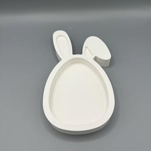 Könnte beinhalten: Weiße Keramik-Schale in Form eines Hasen mit einer großen ovalen Vertiefung in der Mitte. Die Schale ist perfekt für die Aufbewahrung von kleinen Gegenständen wie Süßigkeiten oder Schmuck.
