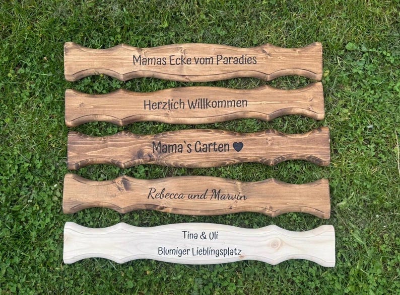 Puede incluir: Una colecci&oacute;n de letreros de madera con bordes decorativos, cada uno grabado con texto. Los letreros son de varios tonos de marr&oacute;n y uno es de color claro. El texto incluye frases como "Mama's Garden" y nombres como "Rebecca y Marvin".