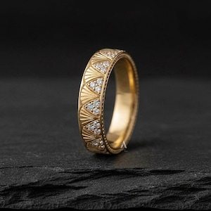 May include: A gold band ring featuring a repeating pattern of engraved fan-shaped motifs. Each fan section is inlaid with small, clear, round-cut stones. The edges of the ring are finished with a delicate beaded texture along the entire circumference.