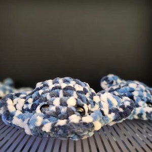 May include: Three handmade plush stingrays in shades of blue, white, and navy. The soft toys have a textured, speckled pattern and small, black eyes. The stingrays are arranged on a metal grate, with a dark background.