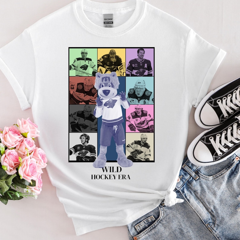 May include: White t-shirt with a colorful graphic of hockey players and a mascot. The graphic includes the text "WILD HOCKEY ERA".