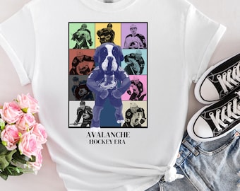 May include: White t-shirt featuring a graphic of a dog wearing a hockey jersey, surrounded by images of hockey players. The text "Avalanche Hockey Era" is printed below the graphic.