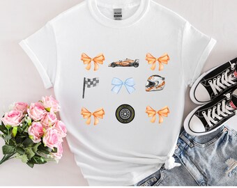 May include: A white short-sleeve t-shirt featuring a graphic print of four orange bows, one light blue bow, a race car, a checkered flag, a racing helmet, and a tire. The design is arranged in a grid pattern on the front of the garment.