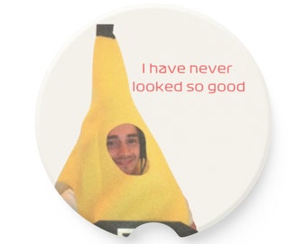 May include: A white ceramic coaster with a yellow banana costume on a person's head. The text "I have never looked so good" is printed on the coaster.