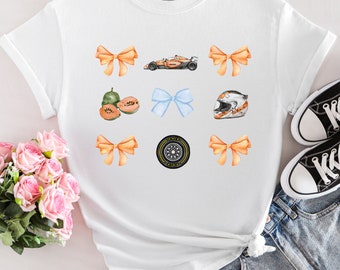 May include: White t-shirt with a variety of colorful illustrations, including a race car, a helmet, a tire, fruit, and bows.