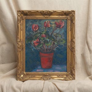 May include: An oil painting of a potted plant with red flowers and green leaves, set against a blue background. The plant is in a red pot. The painting is in a gold ornate frame.