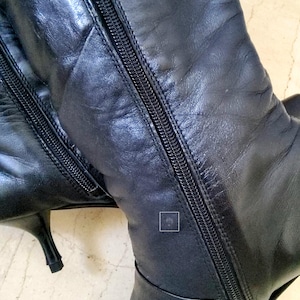 May include: Black leather knee-high boots with a pointed toe and stiletto heel. The boots feature a full-length zipper on the side and are made of a smooth, shiny leather material. The boots are a classic style.