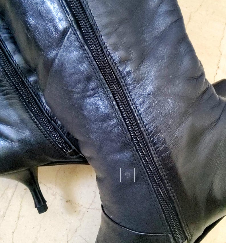May include: Black leather knee-high boots with a pointed toe and stiletto heel. The boots feature a full-length zipper on the side and are made of a smooth, shiny leather material. The boots are a classic style.
