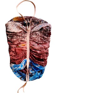 May include: A colorful, patterned top with a drawstring closure and a halter strap. The fabric features a mix of red, brown, blue, and cream hues with paisley and floral designs. The top is gathered and ruched, creating a textured effect.