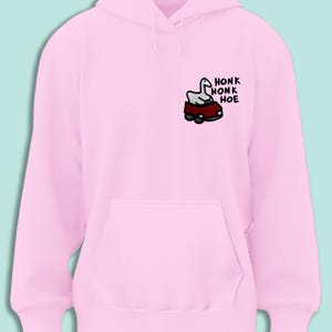 A pink hoodie with a cartoon image of a goose in a car and the text "honk honk hoe" printed on it.