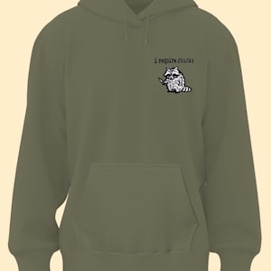 May include: Olive green hoodie with a kangaroo pocket and drawstring hood. The upper left chest features a black and white illustration of a raccoon holding a knife, with the text "i require snacks" above it.
