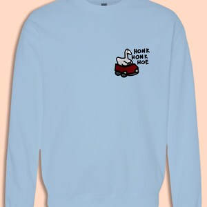 A light blue sweatshirt with a cartoon image of a car and the text "HONK HONK HOE" printed on the front.