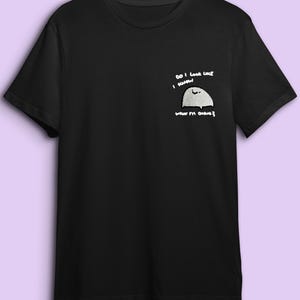 A black t-shirt with a white graphic design on the left side, depicting a small white circle with a black outline and the text "Do I look like I'm going to die?"