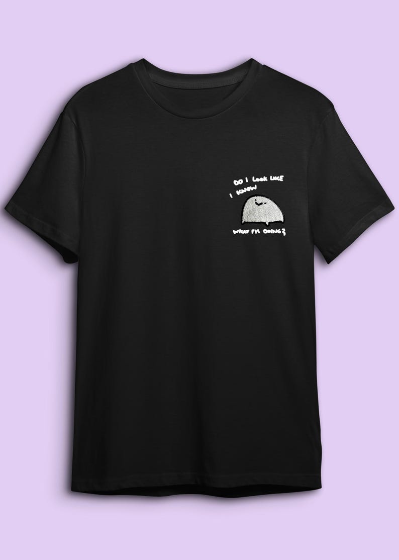 A black t-shirt with a white graphic design on the left side, depicting a small white circle with a black outline and the text "Do I look like I'm going to die?"