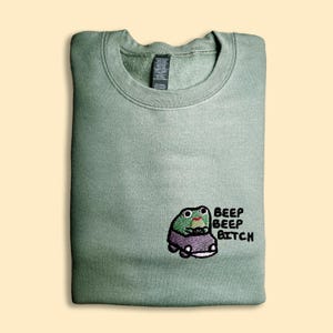 A green sweatshirt with a cartoon frog and the text "BEEP BEP BITCH" printed on it.