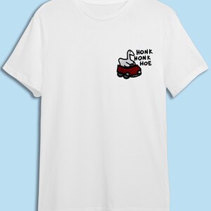 A white t-shirt with a graphic design on the left side depicting a cartoon image of a car with a bird inside.