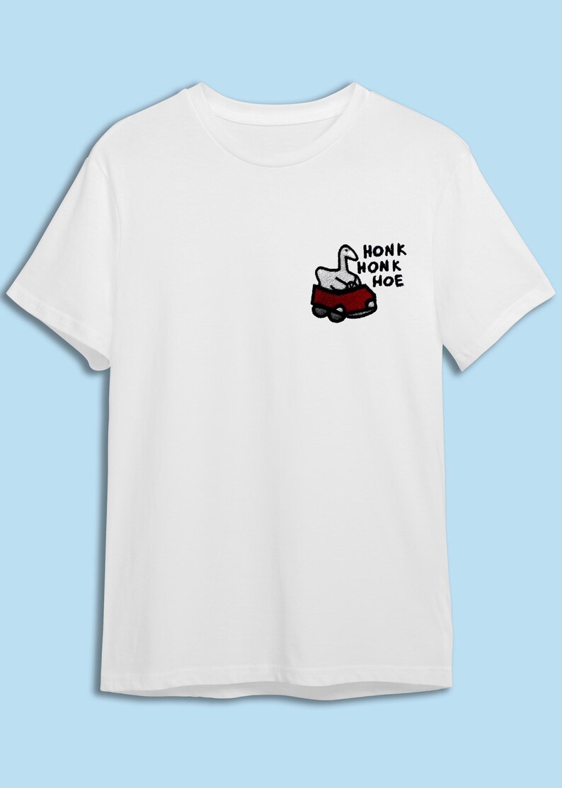 A white t-shirt with a graphic design on the left side depicting a cartoon image of a car with a bird inside.