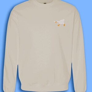 May include: A light beige sweatshirt with a small embroidered image of a white goose holding a carrot in its beak.