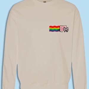 A beige sweater with a colorful graphic design on the front, depicting a cat with a rainbow-colored stripe.