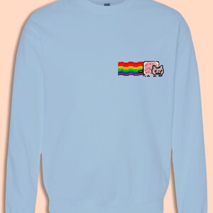 A light blue long-sleeved shirt with a colorful pixelated cat graphic on the left side.