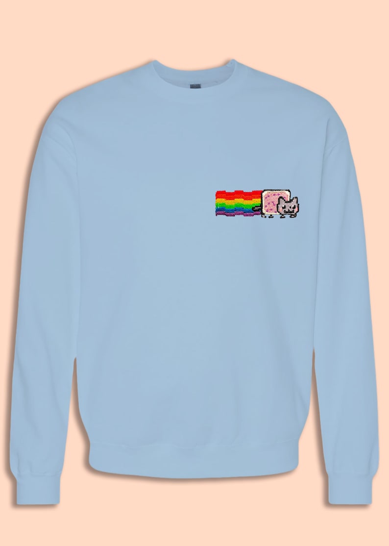 A light blue long-sleeved shirt with a colorful pixelated cat graphic on the left side.