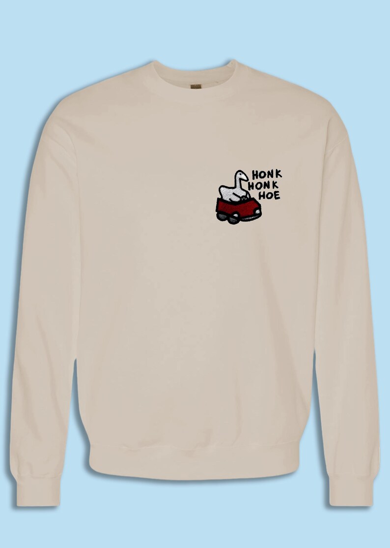 A beige sweater with a small cartoon image of a car and the text "HONK HONK HOE" printed on it.