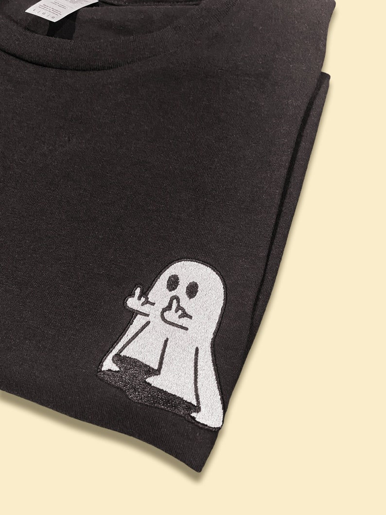 May include: Black t-shirt with a white embroidered ghost giving the middle finger.