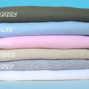 May include: A stack of six folded t-shirts in different colors: green, blue, pink, beige, gray, and white. The colors are labeled in white text.