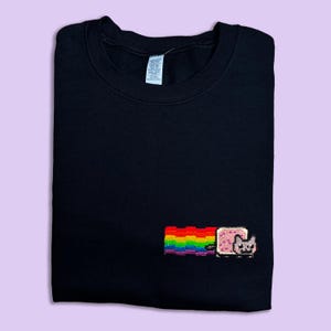 A black t-shirt with a colorful pixel art design of a cat and a rainbow on the front.