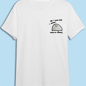 A white t-shirt with a small cartoon character and text printed on it.