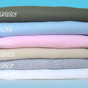 May include: A stack of six folded t-shirts in different colors: green, blue, pink, beige, grey, and white. The colors are labeled in white text.