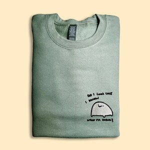 A green sweatshirt with a small cartoon ghost and text printed on it.