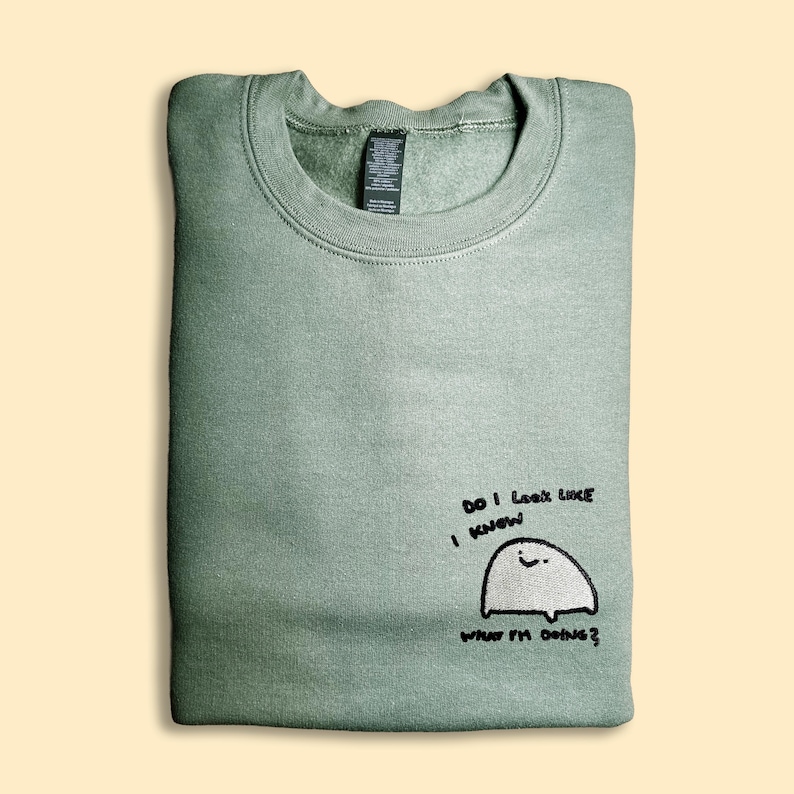 A green sweatshirt with a small cartoon ghost and text printed on it.
