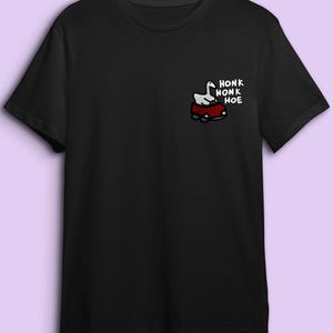 A black t-shirt with a graphic design on the left side depicting a cartoon goose in a red car.