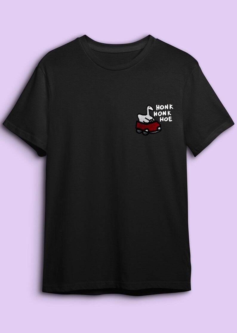A black t-shirt with a graphic design on the left side depicting a cartoon goose in a red car.