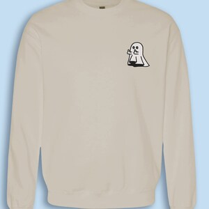 May include: A light beige sweatshirt with a small black and white ghost graphic on the left chest. The ghost is giving a thumbs up.