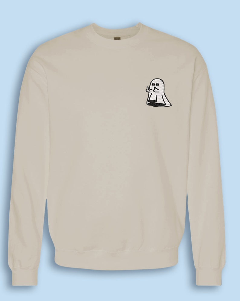 May include: A light beige sweatshirt with a small black and white ghost graphic on the left chest. The ghost is giving a thumbs up.