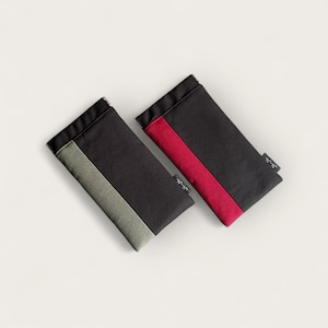 Könnte beinhalten: Zwei schwarze Stoffhüllen mit kontrastierenden Farbstreifen. Die Hülle links hat einen hellgrünen Streifen und die Hülle rechts einen roten Streifen. Beide Hüllen tragen den Schriftzug "Uniqlo".