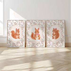 May include: Set of three framed art prints featuring watercolor illustrations of squirrels. Each squirrel is depicted in a different pose, surrounded by a floral border. The artwork has a soft, pastel color palette with a white background.