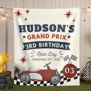 May include: A rectangular fabric banner featuring a vintage red race car, checkered flag patterns, and the text "HUDSON'S GRAND PRIX 3RD BIRTHDAY Race Day September 20th, 2027". The design includes red star accents and a red circle with the number 03.