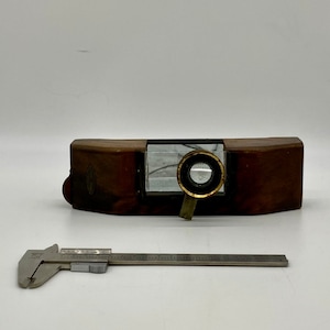 May include: A wooden box with a glass window and a brass magnifying lens. The box is about 10 inches long and 2 inches wide.